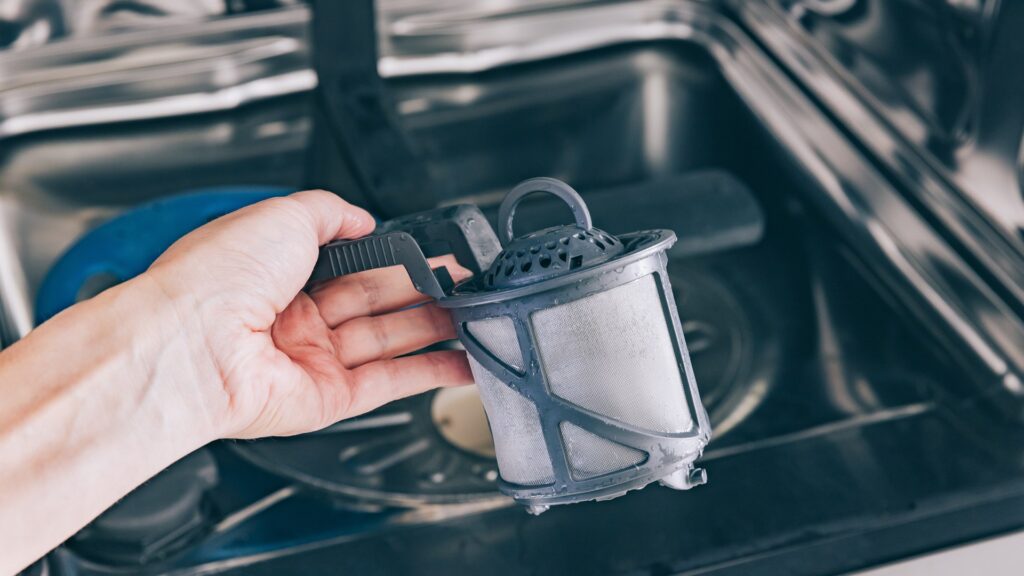 A dishwasher filter assembly lifted out of the sump and held over the open door