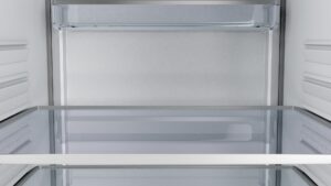 The empty interior of a refrigerator with pale steel walls and glass shelves
