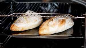 Two loaves of bread baking on a tray inside an oven with the cavity light on